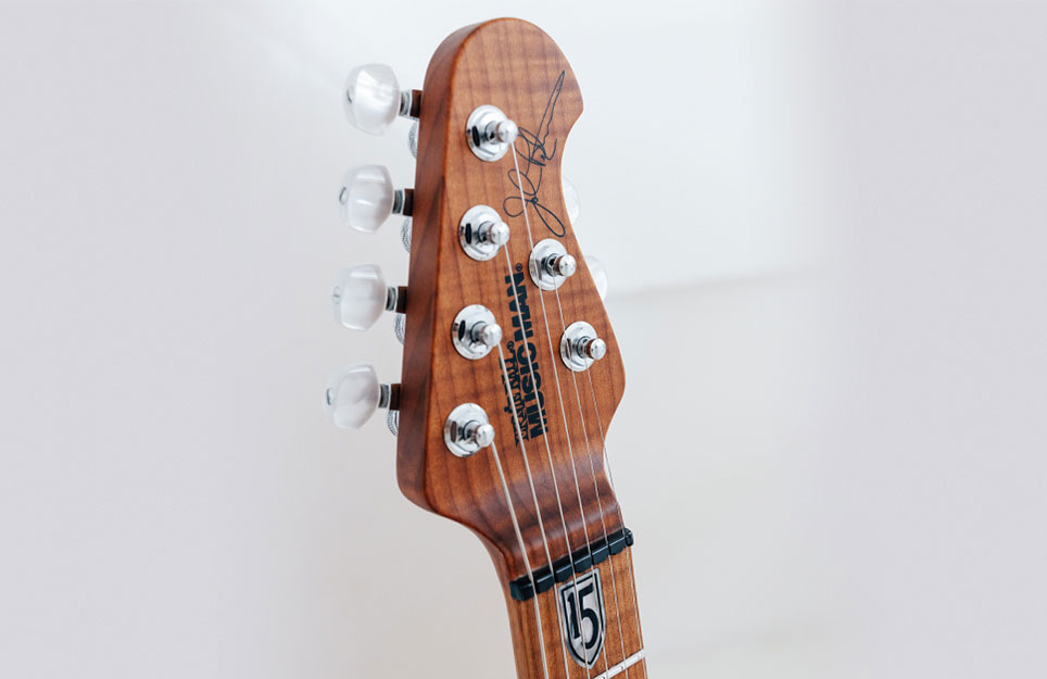 Close-up of a guitar headstock featuring tuning pegs and a signature, with a wooden finish.